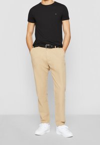 T-shirt nera a maniche corte, pantaloni chinos beige con cintura e sneakers bianche. Design semplice, texture liscia e colori classici.