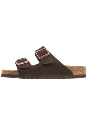 Ciabatte in suede marrone con due cinturini regolabili, fibbie color rame e un sottopiede in sughero. Suola piatta con design della trama testurizzato.