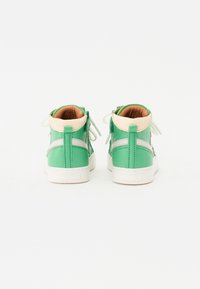 Hoogtop sneakers met een groene leren bovenkant, beige accenten, een witte rubberen zool en groene veters. Achteraanzicht toont stikdetails.