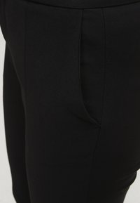 Černé kalhoty na míru vyrobené z hladké látky se slim fit střihem. Obsahují boční kapsy a precizní švy podél švů.