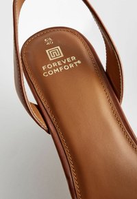 Sandal in pelle marrone con soletta imbottita, caratterizzata da una marcatura dorata e una cucitura dettagliata ai lati. Etichetta della taglia visibile come "40."