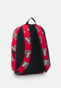 Mochila roja y negra con el logo de Nike. Diseño acolchado, correas dobles para los hombros y un bolsillo frontal con cremallera para almacenamiento. Tejido texturizado.