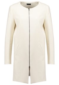 Gräddfärgad kappa med en lång, rak design, fickknäppning fram och två sidofickor. Tillverkad av ett slätt, syntetlädermaterial.