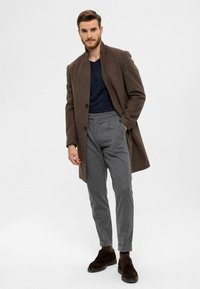 Manteau en laine marron, chemise bleu marine, pantalon gris et chaussures marron foncé. Coupe ajustée, design classique, aspect sur mesure avec manches retroussées et boutons.