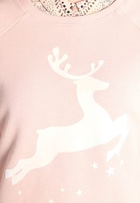 Sudadera rosa claro con un gráfico de un reno blanco saltando, con cuernos y estrellas. Tejido suave con un corte holgado y escote acanalado.