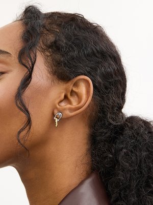 Lähikuva naisen korvasta, jossa on hopea- ja kultainen rengaskorvakoru, tummat kiharat hiukset sidottuna taakse ja löysä edestä kihara.