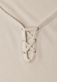 Tissu beige avec un gros plan d'un décolleté en V avec un laçage croisé passé à travers des œillets métalliques.