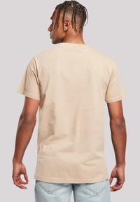 Beige cotton t-shirt, crew neck, short sleeves, plain design without patterns. Worn with light blue jeans, showcasing a relaxed fit.