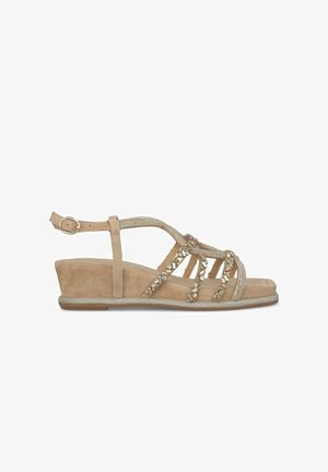 Sandale compensée beige en matériau suédé, avec des accents en perles et une bride de cheville ajustable. Elle possède une semelle intérieure texturée et un talon renforcé.