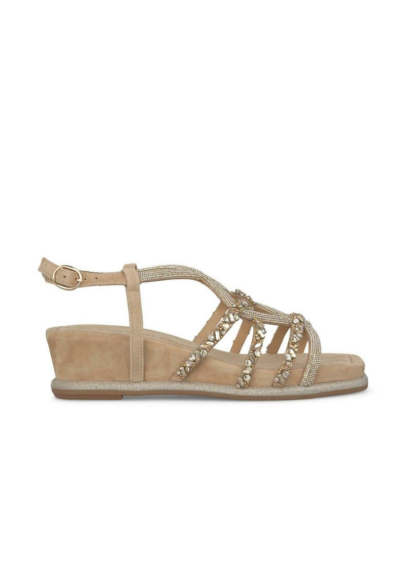 Sandale compensée beige en matériau suédé, avec des accents en perles et une bride de cheville ajustable. Elle possède une semelle intérieure texturée et un talon renforcé.