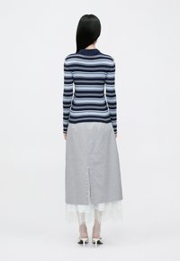 Μπλούζα με μακριά μανίκια σε ναυτικό μπλε και ανοιχτό μπλε ριγέ, συνδυασμένη με γκρι μακριά φούστα με άνοιγμα στο πίσω μέρος και άσπρη δαντέλα στο τελείωμα, φορεμένη με άσπρα τακούνια.