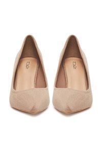 Par de zapatos de tacón alto de punta fina para mujer en ante beige, vistos desde arriba sobre fondo blanco.
