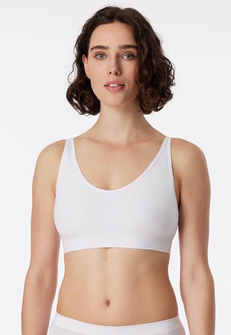 Fehér vezeték nélküli bralette mély dekoltázzsal és széles pántokkal. Puha, sima anyagból készült; a varratmentes kialakítás és az elasztikus szalag jellemzi.