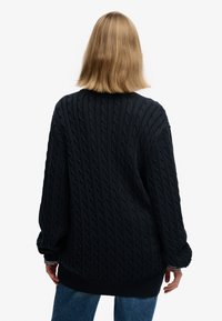 Dark blue cable-knit oversized sweater with a ribbed hem and cuffs, featuring a textured pattern and relaxed silhouette.