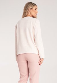 Wpleciony jasnoróżowy sweter z teksturowanym wzorem, okrągłym dekoltem i długimi rękawami, połączony z pasteloworóżowymi spodniami.