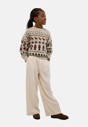 Pull en tricot beige avec motifs multicolores de rennes et flocons de neige ; associé à un pantalon large crème et des bottines marron.