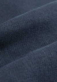 Gros plan d'un tissu tricoté bleu foncé montrant une texture fine, légèrement surélevée et des plis doux.