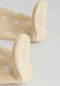 Maniques de four en tissu matelassé beige avec de petits motifs de fleurs blanches sur une surface claire.