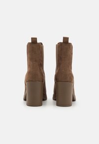 Botines de ante marrón con tacones de bloque, que cuentan con paneles laterales de elastano y lengüetas para poner y quitar fácilmente. Textura suave, diseño elegante.