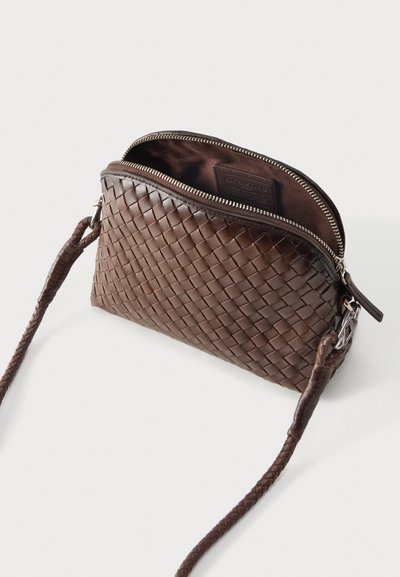 Καφέ πλεκτή δερμάτινη τσάντα χιαστί με ασημένιο φερμουάρ, ανοιχτή κορυφή και ταιριαστό πλεκτό λουρί σε λευκό φόντο.