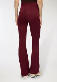 Bordowe leginsy dzwonowe z wysokim stanem, wykonane z elastycznej tkaniny, o gładkiej strukturze i dopasowanej sylwetce.
