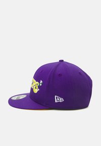 Gorra morada con un ala plana, que presenta texto amarillo bordado y acentos florales, y un logo blanco en el lateral. Textura de tela suave.