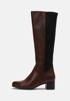 Høj brun skindstøvle til kvinder med sort elastisk ribbet bagpanel og lav blokhæl.