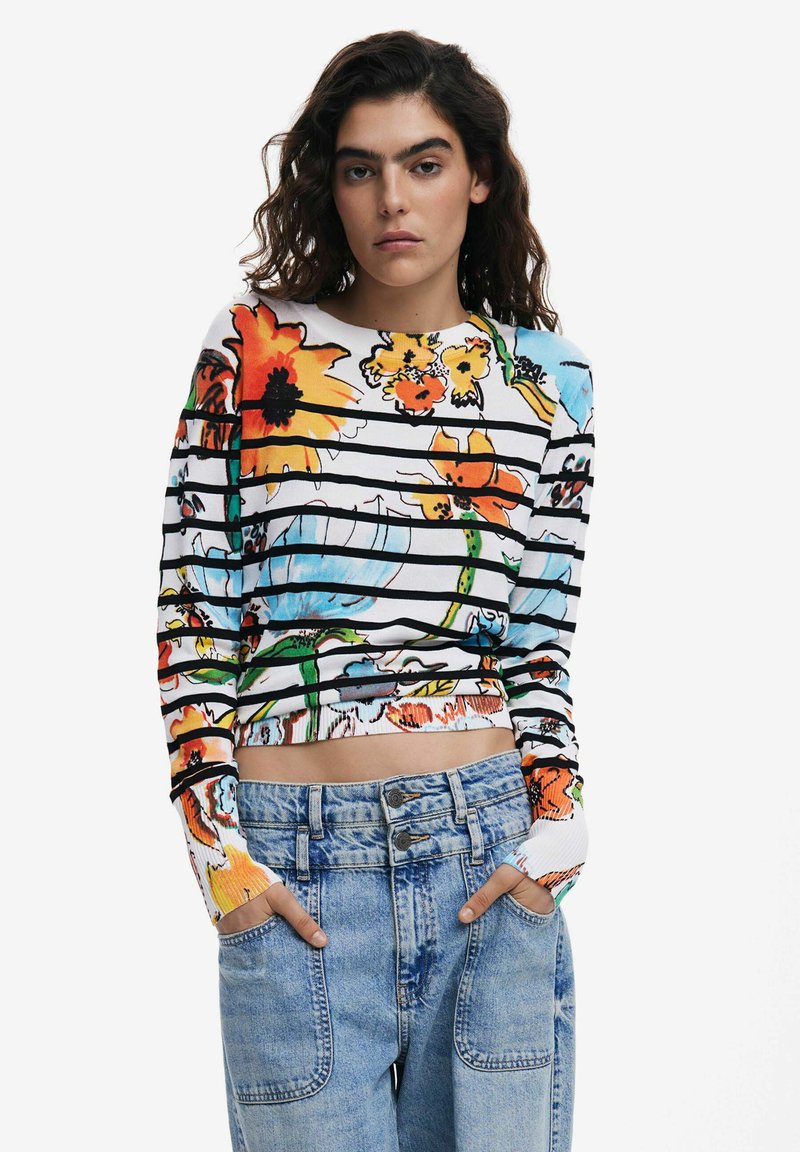 Langärmliges florales Oberteil mit leuchtenden Farben und schwarzen Streifen, aus leichtem Stoff gefertigt. Kombiniert mit hochgeschnittenen blauen Jeans.