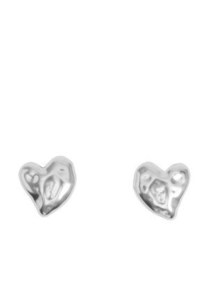 Dwa małe, nieregularnie kształtne błyszczące srebrne kolczyki w kształcie serca na białym tle.