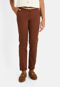 Chinos en coton marron avec une coupe slim, dotés de poches latérales et de poignets retroussés. Associés à des mocassins en daim marron et une ceinture tressée.