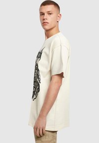 Creme kortærmet T-shirt med et stort sort grafisk design på forsiden, i en afslappet pasform og blødt bomulds materiale.