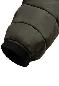 Manica di giacca imbottita verde scuro con trapuntatura orizzontale, polsino elastico nero e texture liscia. Materiale leggero e isolante.