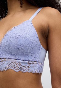 Μπραλέτα από ανοιχτό μωβ δαντέλα με λουλουδάτα σχέδια, ρυθμιζόμενες τιράντες και ανάγλυφη δαντέλα με κυματιστό τελείωμα στο κάτω μέρος. Βάση από απαλό ύφασμα.