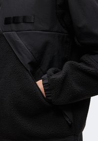 Κοντινό πλάνο ενός ατόμου που φοράει μαύρο φλις μπουφάν με τσέπη με φερμουάρ, με το χέρι σε μέρος της τσέπης.