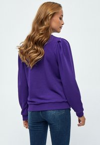 Lila sweatshirt med avslappnad passform, som har puffärmar och ribbade muddar och fåll. Matchas med mörkblå jeans i texturerat tyg.