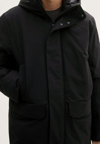 Mustem isoleeritud parka kapuutsiga, millel on tõmblukk ees, kaks suurt esmakotti ja sile, mati viimistlusega pind.