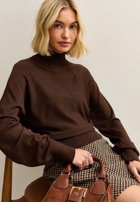 Bruine coltrui met geribbelde boorden, gecombineerd met een geruite rok en een bruine handtas met leren accenten.