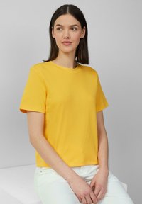 T-shirt en coton jaune avec un col rond et des manches courtes, présentant une coupe décontractée et une texture lisse.