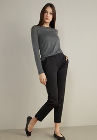 Grå långärmad topp i kombination med svarta smala byxor. Byxorna har sidfickor och slitsar vid fållen. Modellen bär svarta slip-on skor.