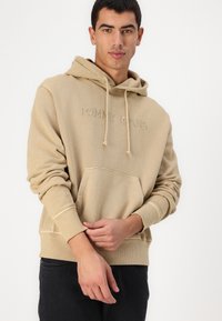 Felpa beige con tasca frontale e cappuccio regolabile con coulisse. Presenta un logo ricamato sul petto. Tessuto morbido con polsini a coste.