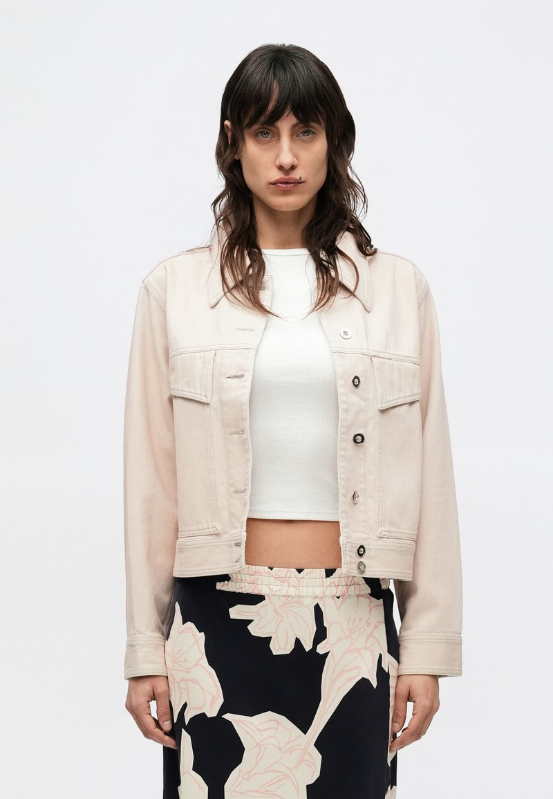 Σακάκι από ροζ τζιν με κοντό σχέδιο, μπροστινές τσέπες, κούμπωμα με κουμπιά και μακριά μανίκια, συνδυασμένο με λευκό τοπ και φούστα με σχέδια.