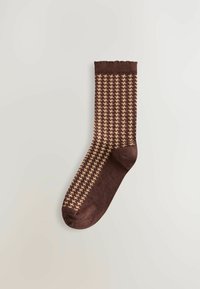 Bruine sok met een pied-de-poule patroon in crème, tentoongesteld op een lichte achtergrond, wat het ontwerp en de textuur benadrukt.