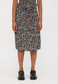 Blomstermidiskjørt med svart bakgrunn og flerfargede blomster, justerbar knyting i livet, og lett stoff. Kombinert med svarte sko.