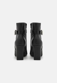 Czarne skórzane botki za kostkę na słupku, z zapięciem na zamek błyskawiczny oraz ozdobnym paskiem z okrągłym srebrnym akcentem.