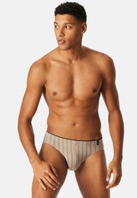 Männer Schwimmbrieftaschen in einem beige-braunen gestreiften Design, mit einem tief sitzenden Schnitt und einem schwarzen elastischen Bund. Glatte Stofftextur.