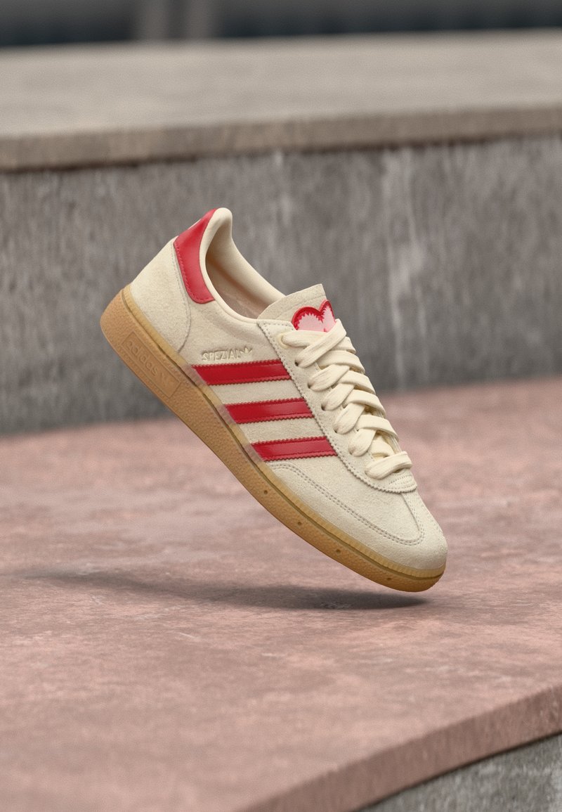 Beige suede sneaker with red accents, featuring three stripes, a heart logo on the heel, and a gum rubber sole.