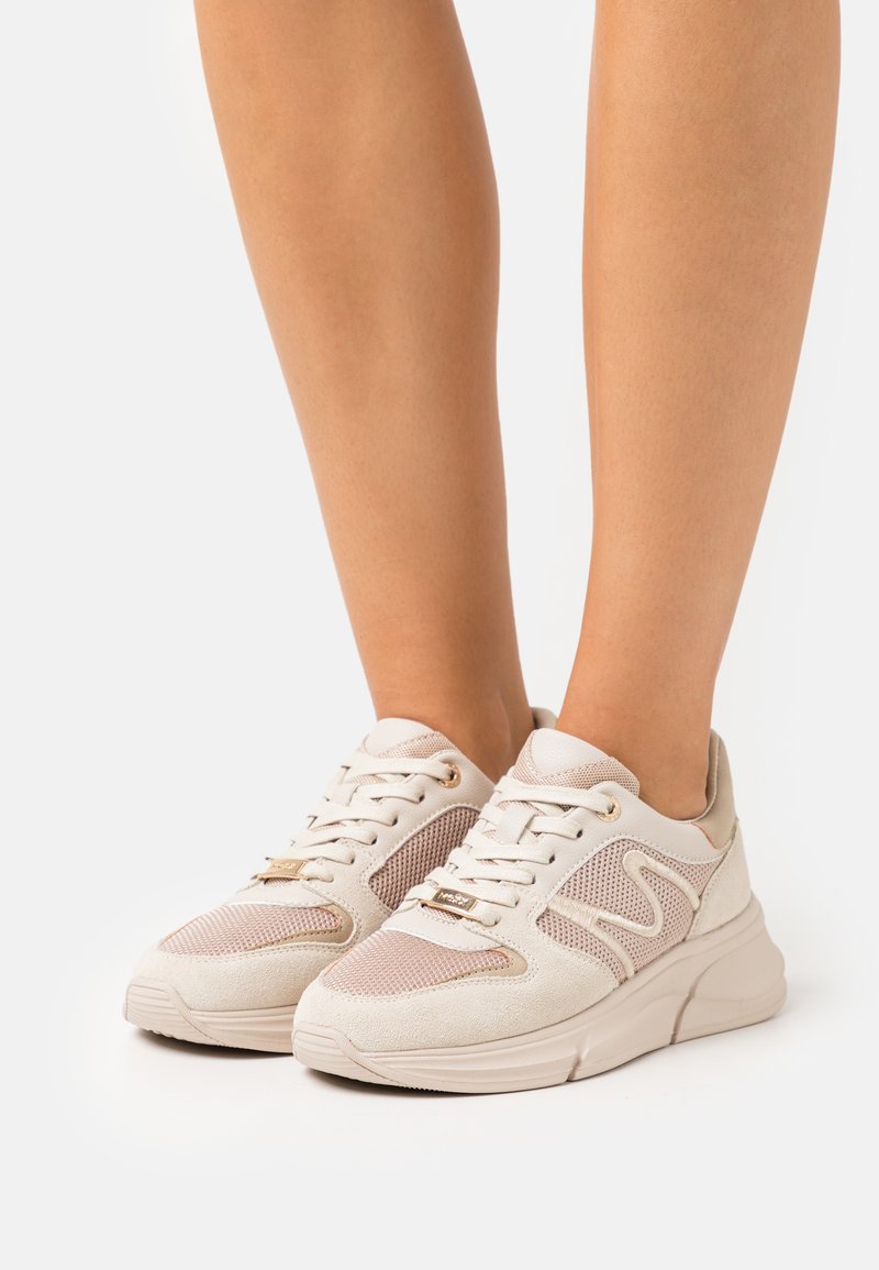 White and beige sneakers with a textured suede and mesh upper, featuring gold-tone accents and a chunky sole design.