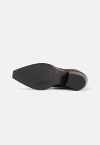 Semelle d'une chaussure habillée en cuir marron montrant un bout pointu et une semelle extérieure en caoutchouc noir texturé avec un talon empilé.
