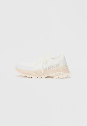 Witte sport sneaker met een gestructureerde stoffen bovenkant, beige zool en een gedrukt logo aan de zijkant. Voorzien van zachte veters en een trekkertje.