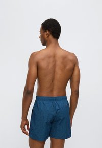 Μαγιό σορτς σε σκούρο μπλε με μοτίβο φύλλων, διαθέτει ελαστική μέση και πίσω τσέπη. Υφασματικό υλικό που είναι απαλό και ελαφρύ.